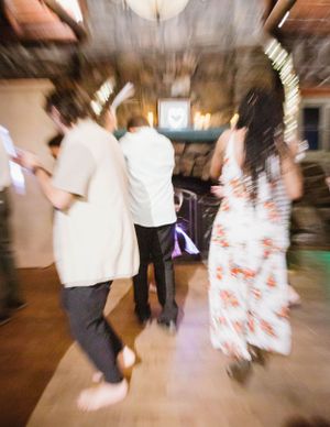 Motion-blurred shot of people dancing at an indoor party or celebration with a floral dress visible in the background.
