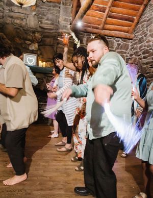 Wedding guests dance and celebrate on a rustic wooden dance floor inside a stone-walled venue.