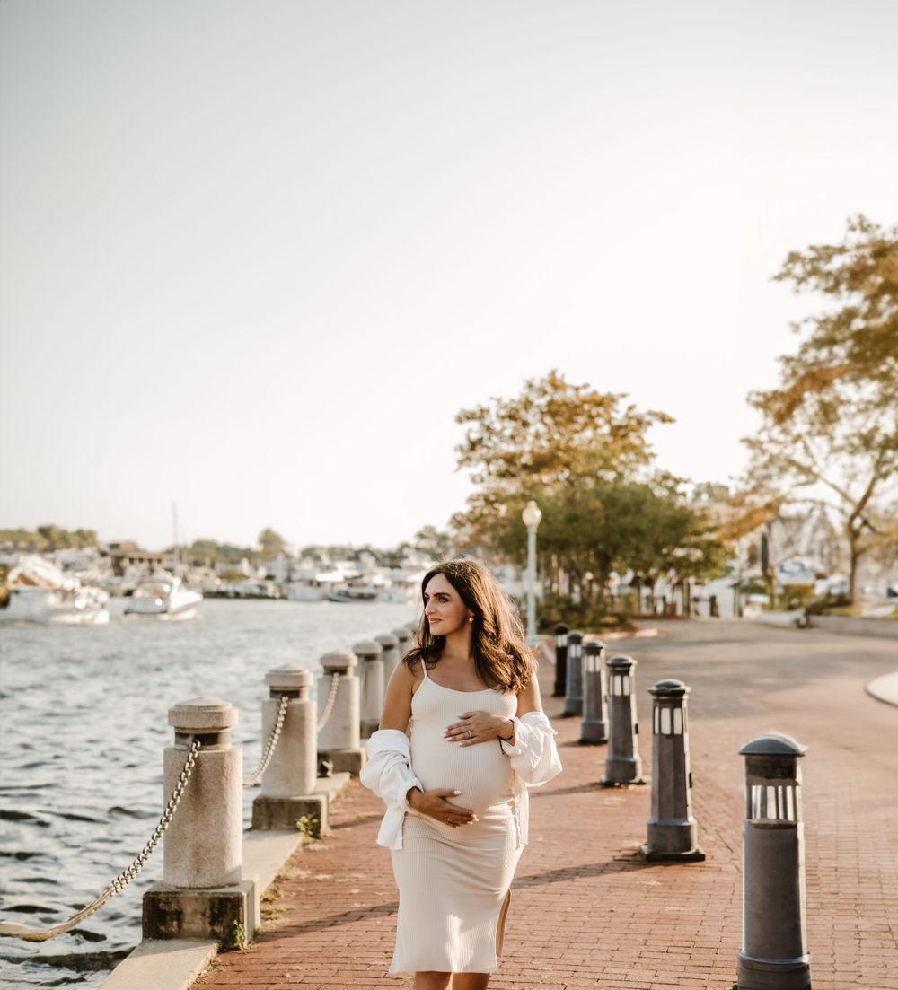 Person in elegant white dress poses along a waterfront promenade during golden hour.