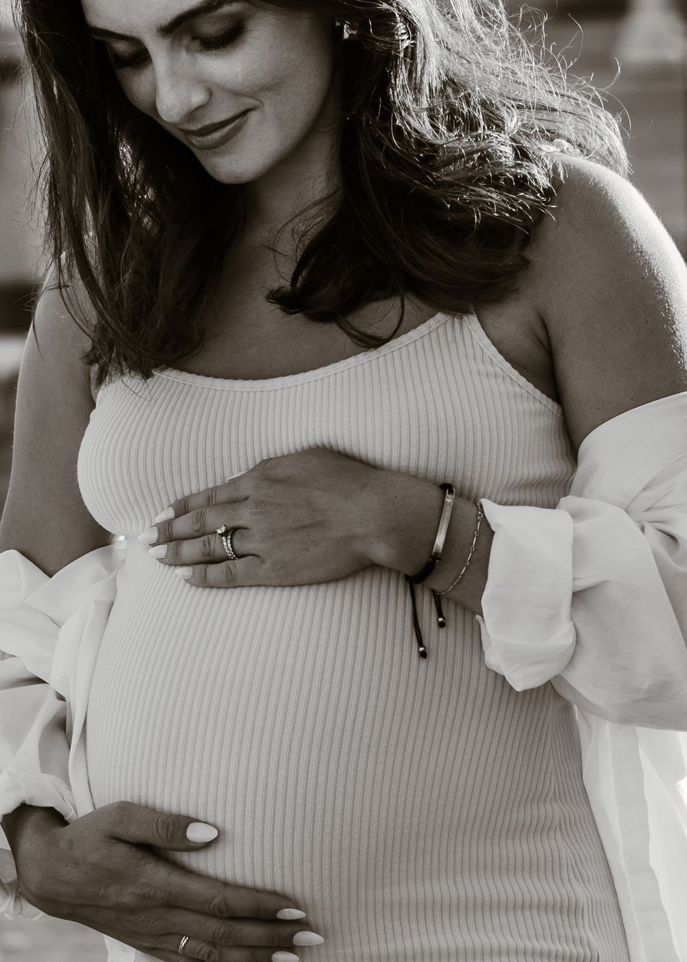 Black and white portrait of expectant mother holding belly while wearing white ribbed dress.