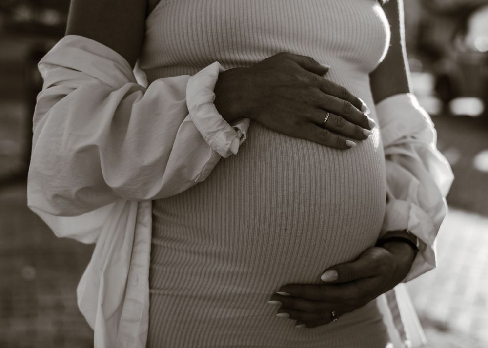 Black and white close-up of hands tenderly cradling pregnant belly in ribbed dress.