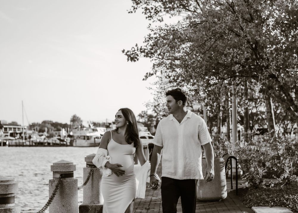 Black and white maternity photo of couple strolling along marina walkway.