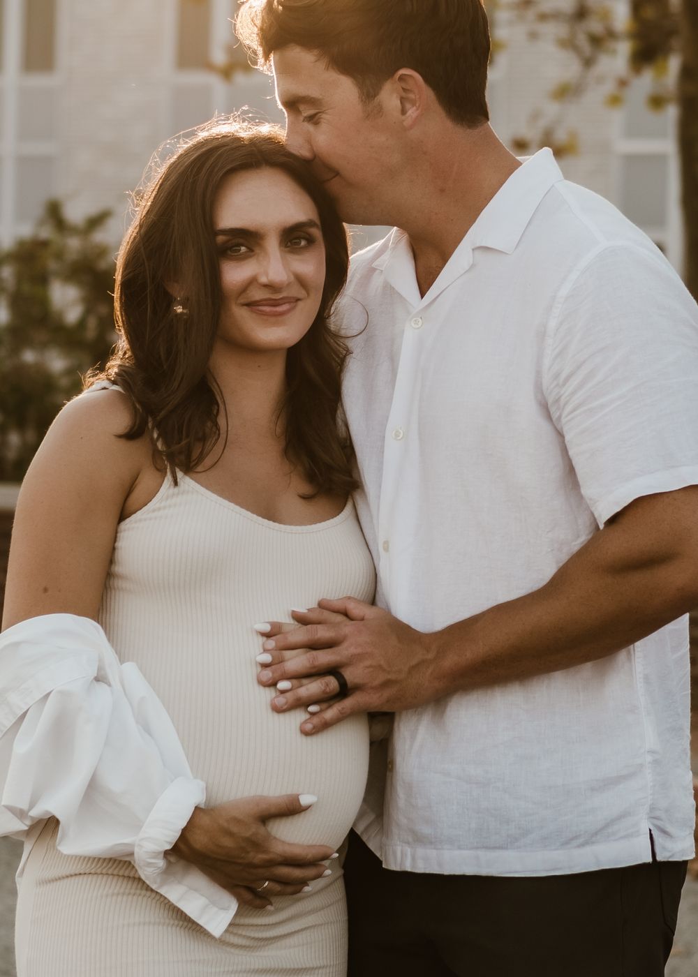 Couple in white clothing sharing tender moments during a sunset photoshoot.
