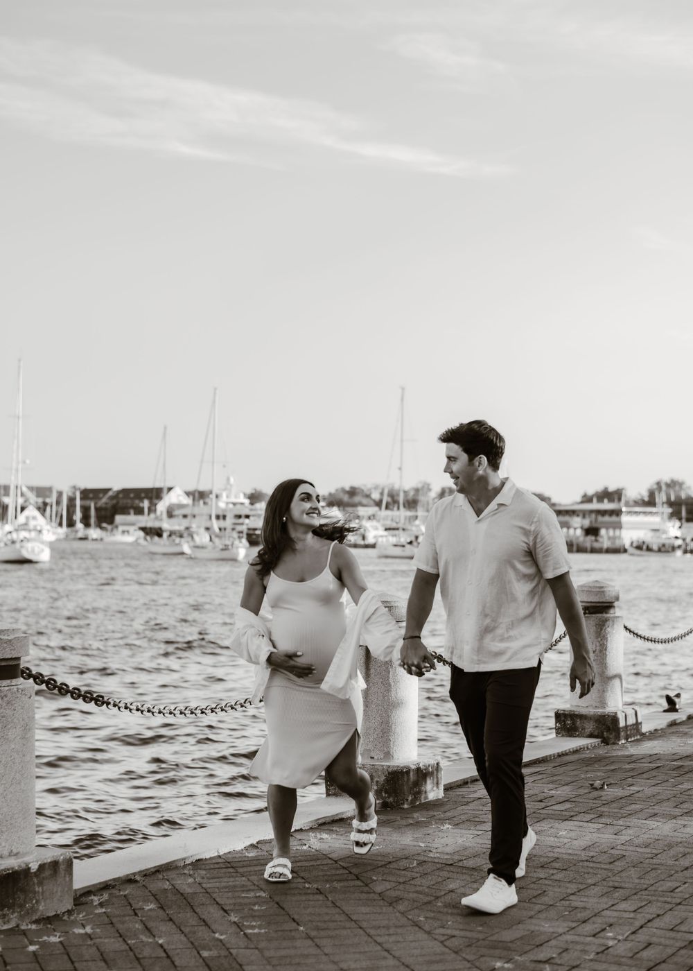 Black and white photo of a couple walking along a waterfront promenade.