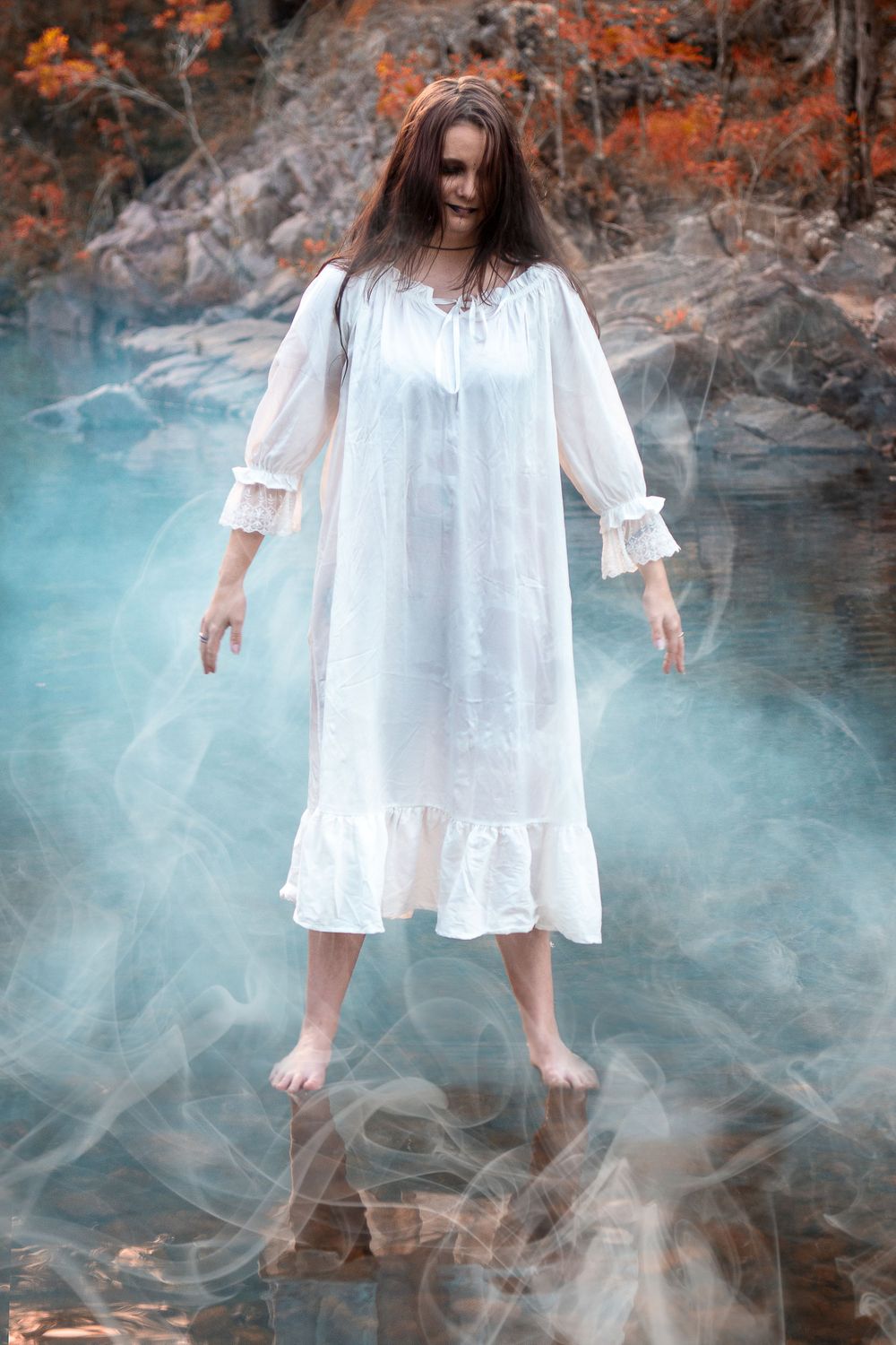 Ethereal figure in white dress floating over misty turquoise water surrounded by autumn foliage.