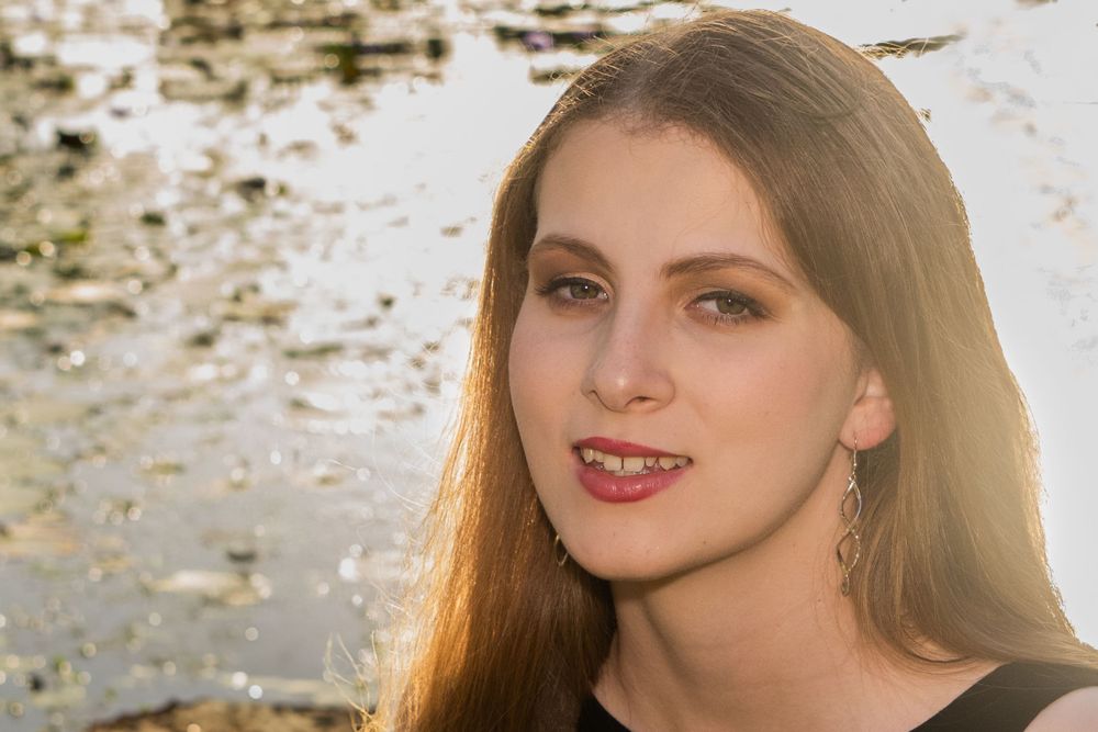 Portrait shot with golden sunlit hair against a blurred natural backdrop with water reflections.