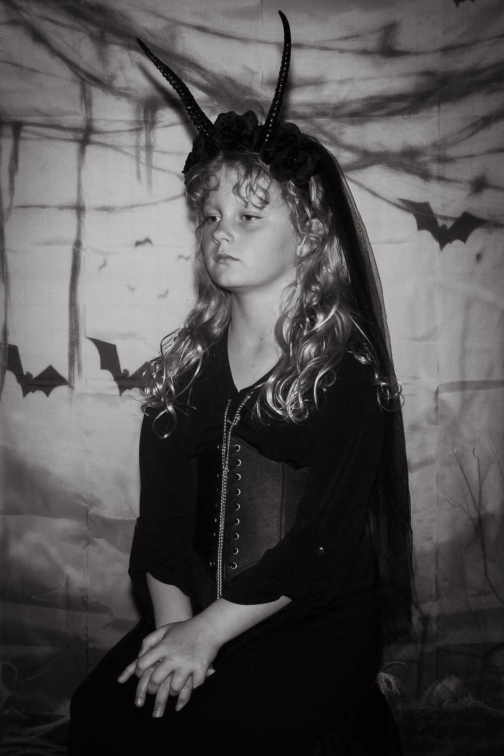 Black and white Halloween portrait with dramatic lighting, horns, and bats against a spooky backdrop.