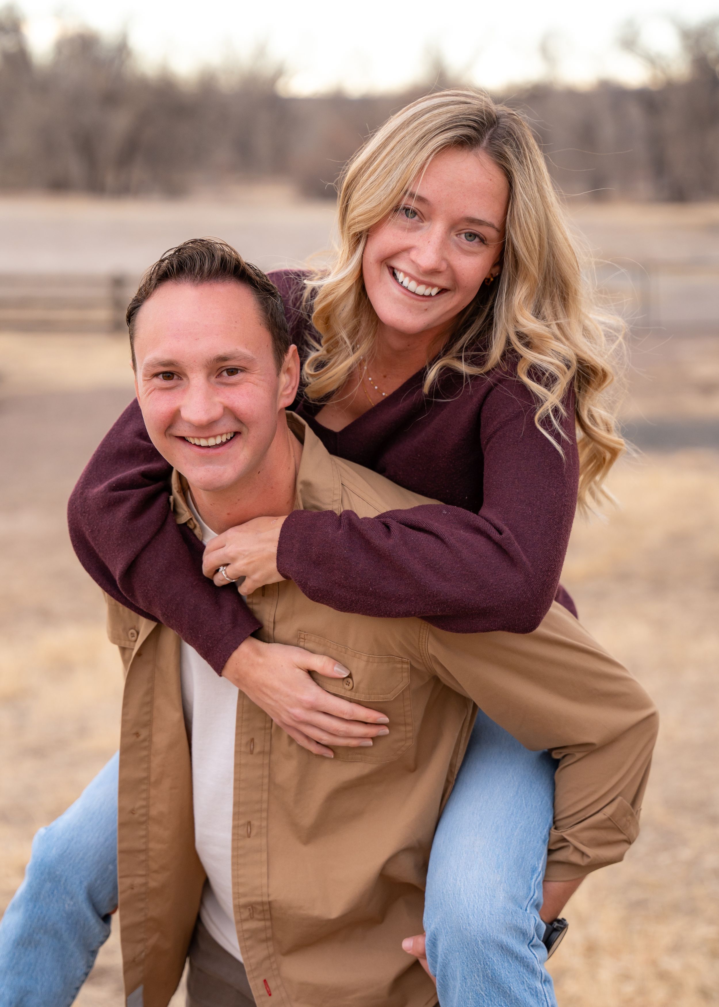 Happy couple smiling and embracing outdoors on an autumn day, with one giving a piggyback ride to the other.