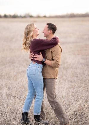 A romantic couple embrace and laugh together in a golden autumn field during sunset.