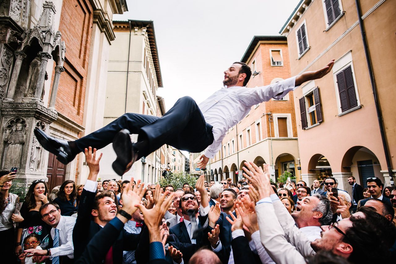 Joyful wedding celebration in an Italian street with guests tossing confetti.