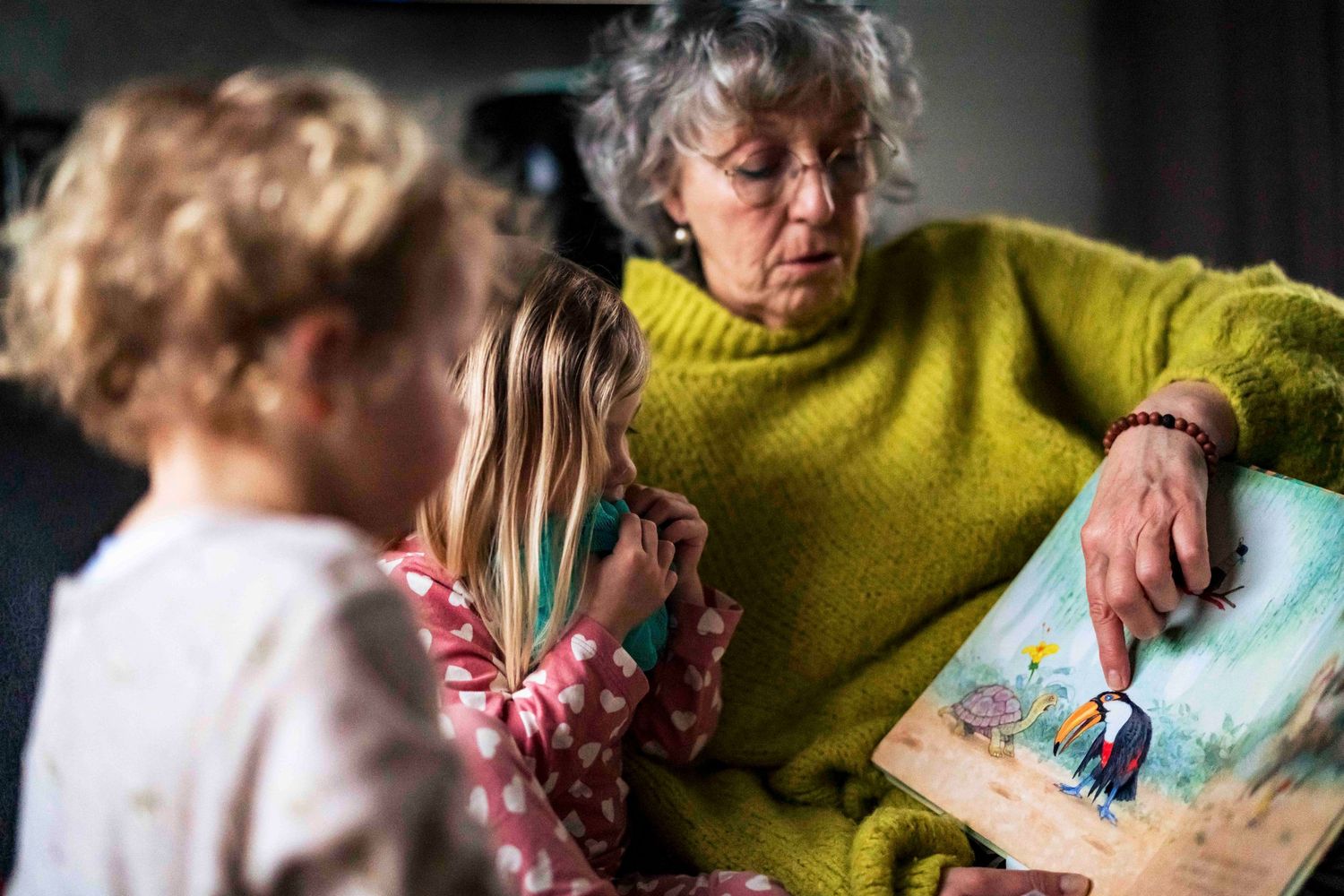A person in yellow sweater reading a storybook to children.