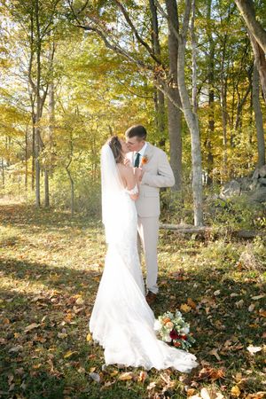 Bride and groom share a kiss in an autumn forest surrounded by golden fallen leaves.