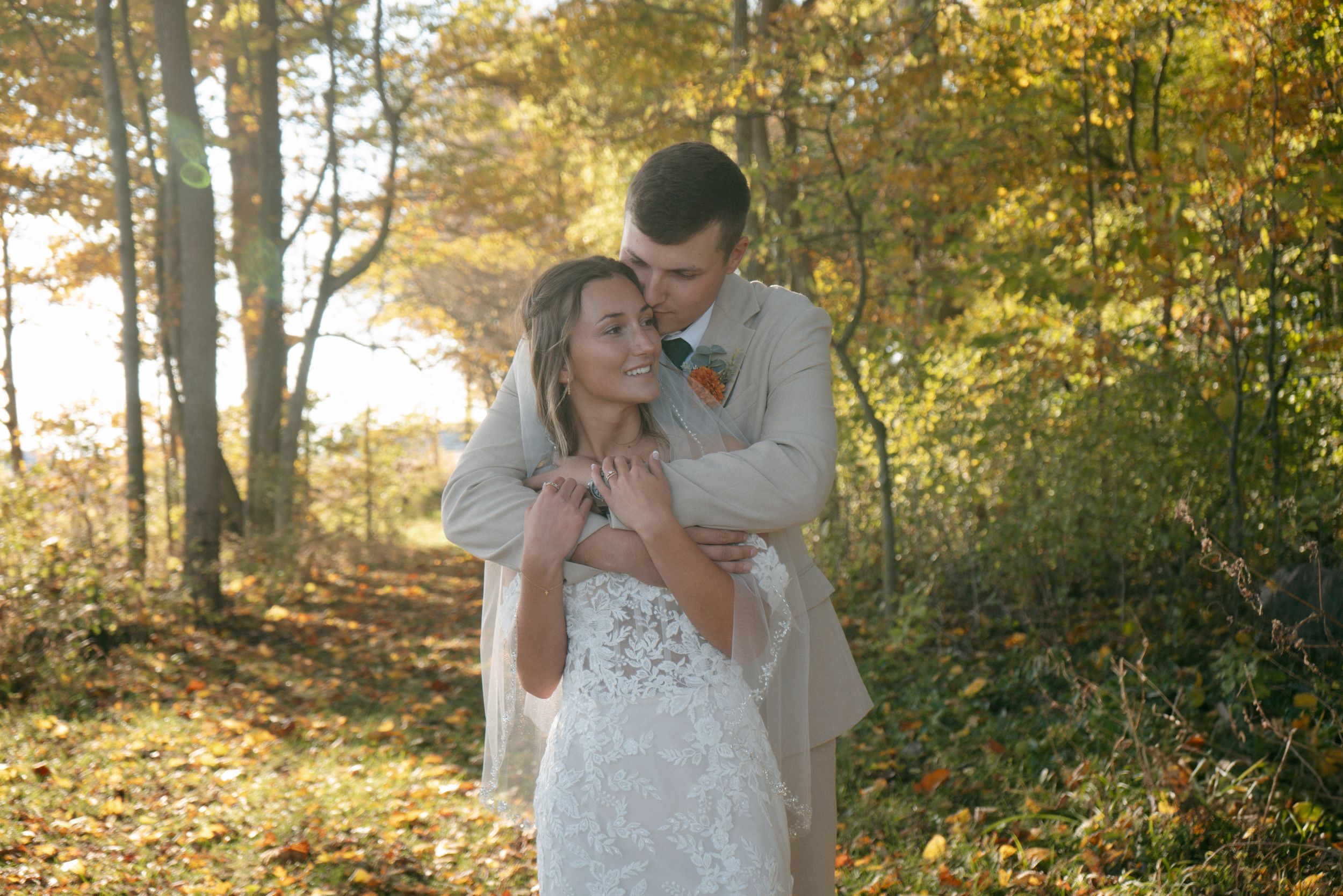 Romantic couple in wedding attire embracing in a sunlit autumn forest with golden foliage.