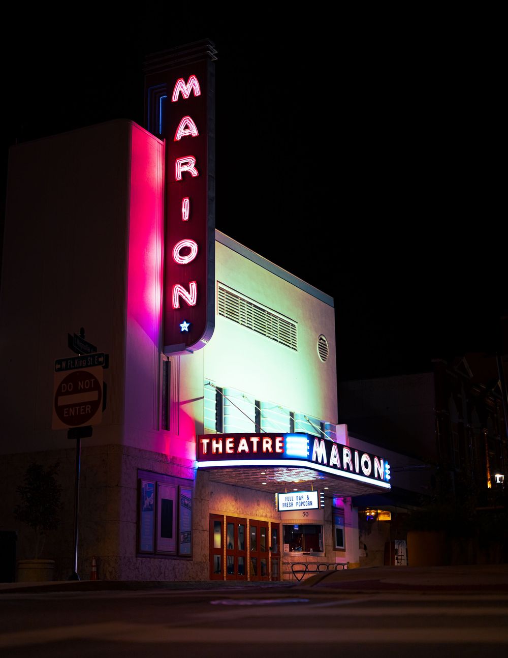 Marion Theatre lit up with vibrant pink neon signs at night, showcasing its classic Art Deco architecture.