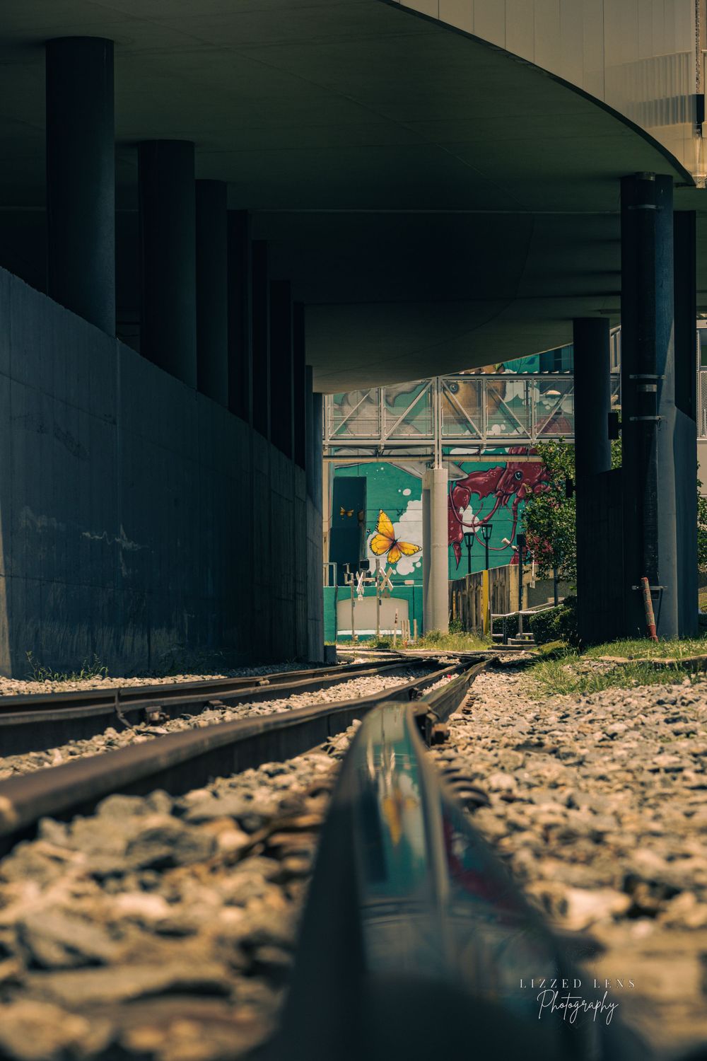 Railroad tracks recede under a curved overpass toward colorful street murals in urban setting.
