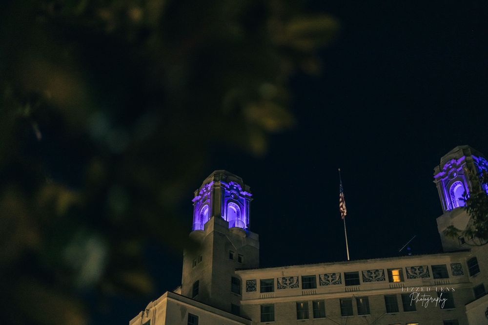 Historic building with purple-lit towers against a dark night sky with an American flag.