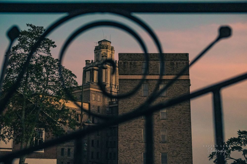 Historic stone tower building framed through ornate iron gate scrollwork at sunset.