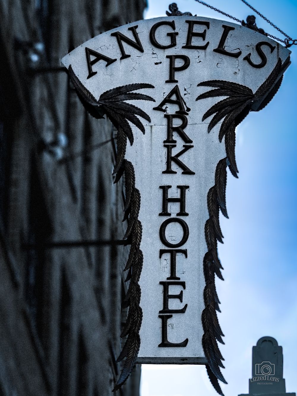 Vintage Angel's Park Hotel sign with ornate black ironwork against a blue sky.