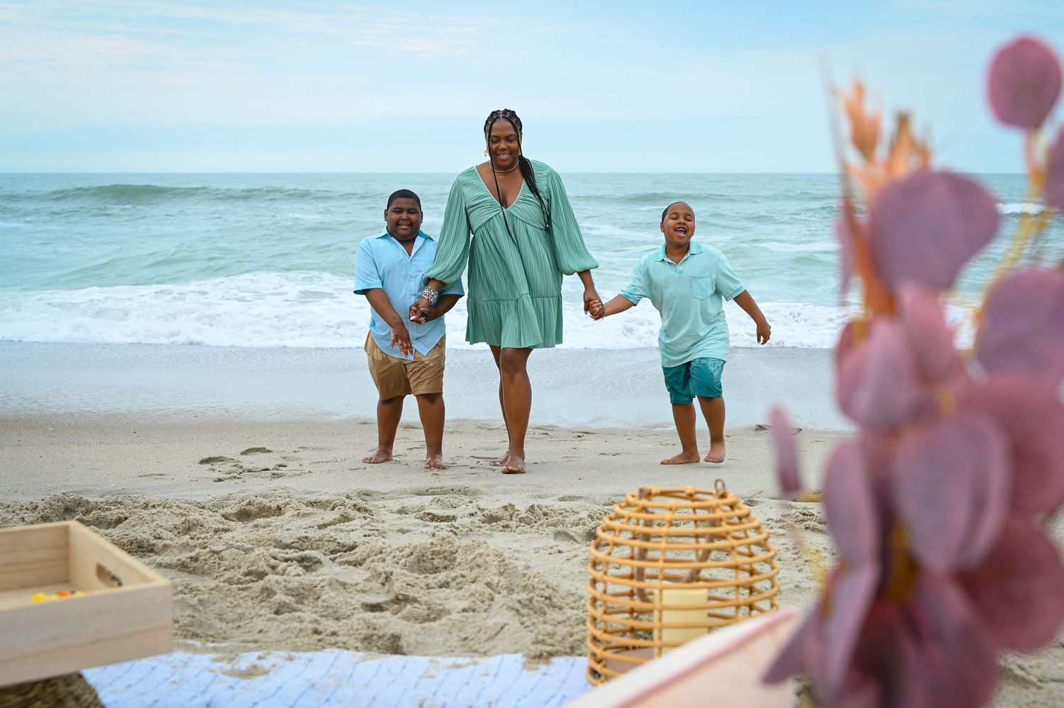 Three people walk along the beach with a picnic setup in the foreground.