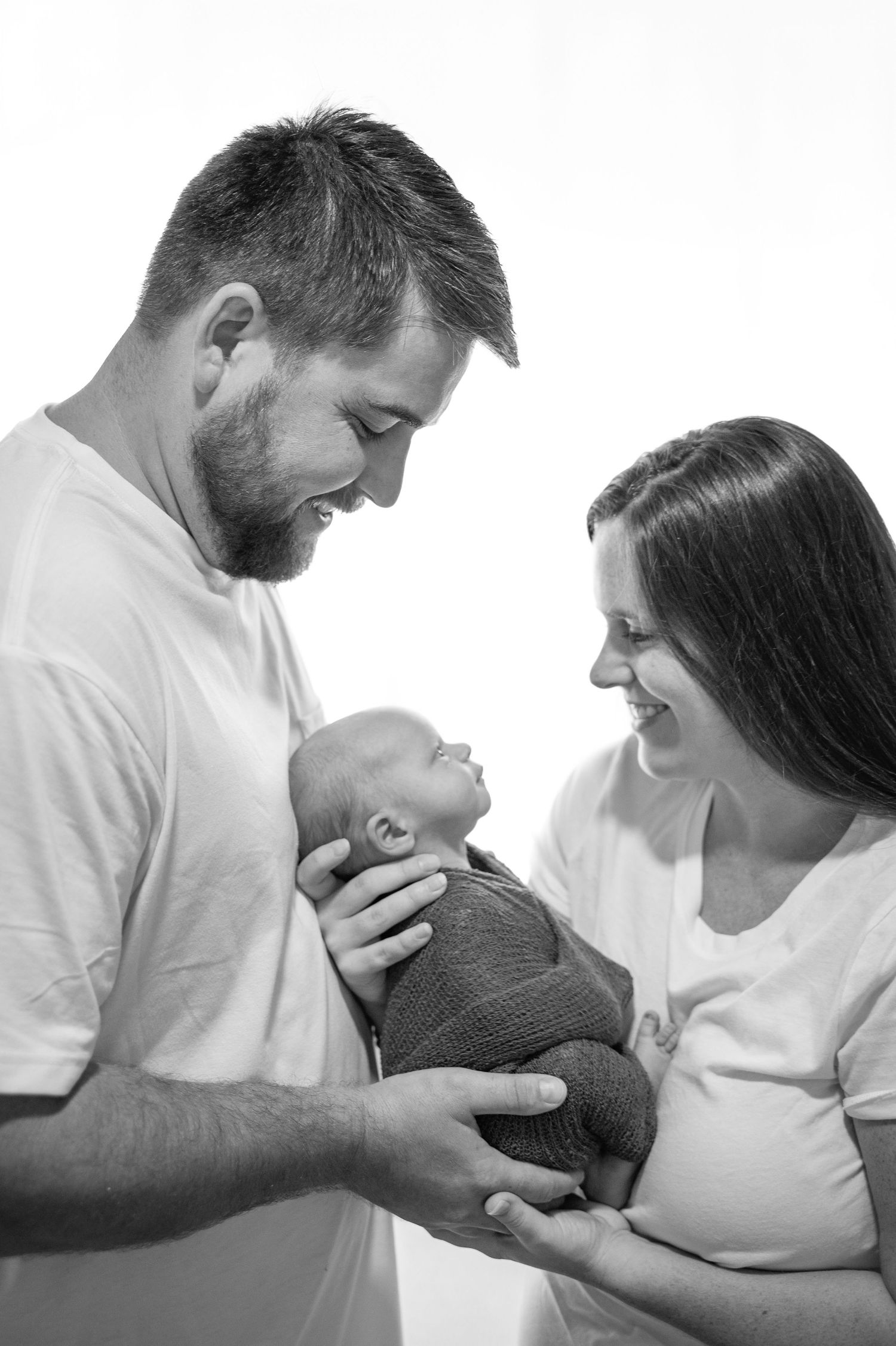 Black and white Family Portrait for Wilmington Locals tenderly holding a swaddled newborn baby during a Newborn Photoshoot.