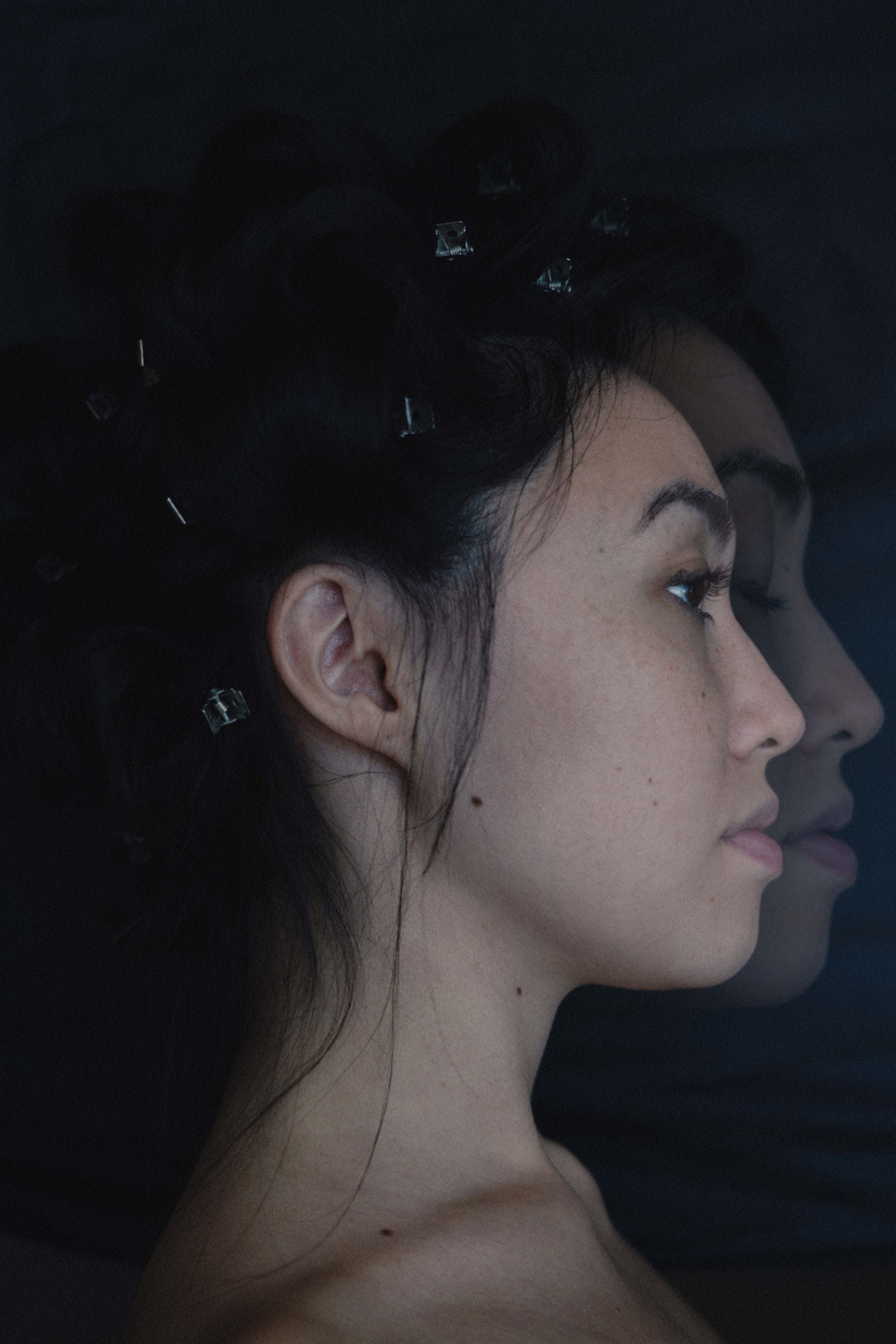 Artistic portrait of a woman in profile with hair clips, reflected in a dark surface.
