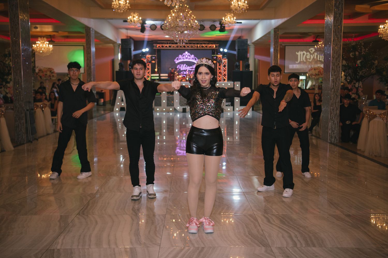 Group of people dancing in an elegant venue with chandeliers and colorful lighting.