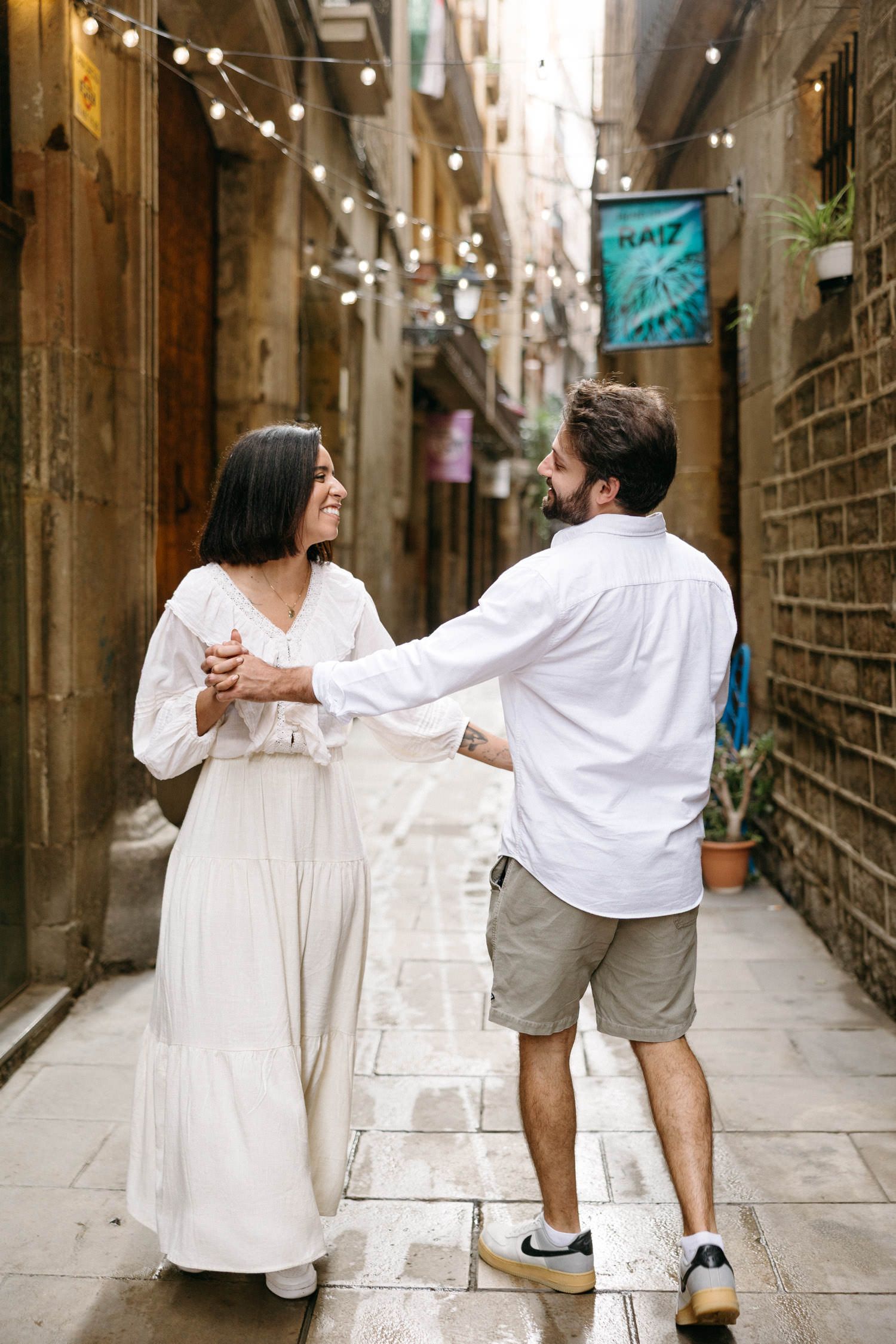 A couple sharing a romantic dance in a narrow alley decorated with string lights.