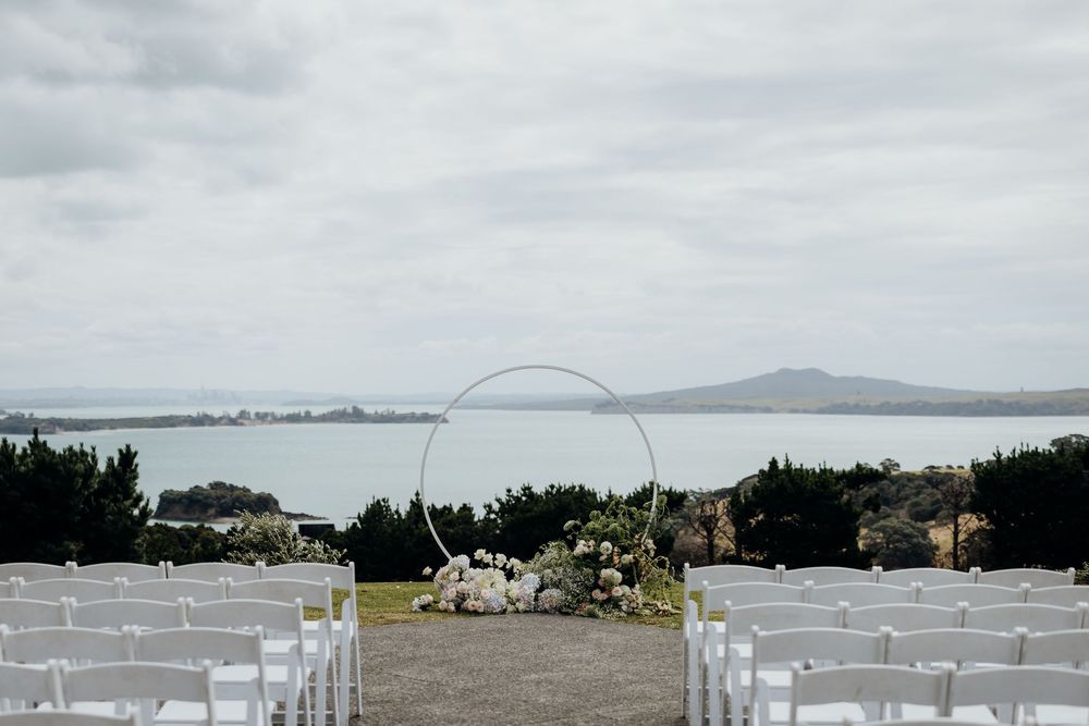 Wedding ceremony setup with white chairs and floral arch overlooking a coastal bay view.