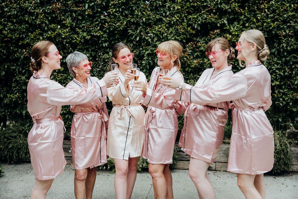 A group wearing matching pink satin robes laughing together outdoors.