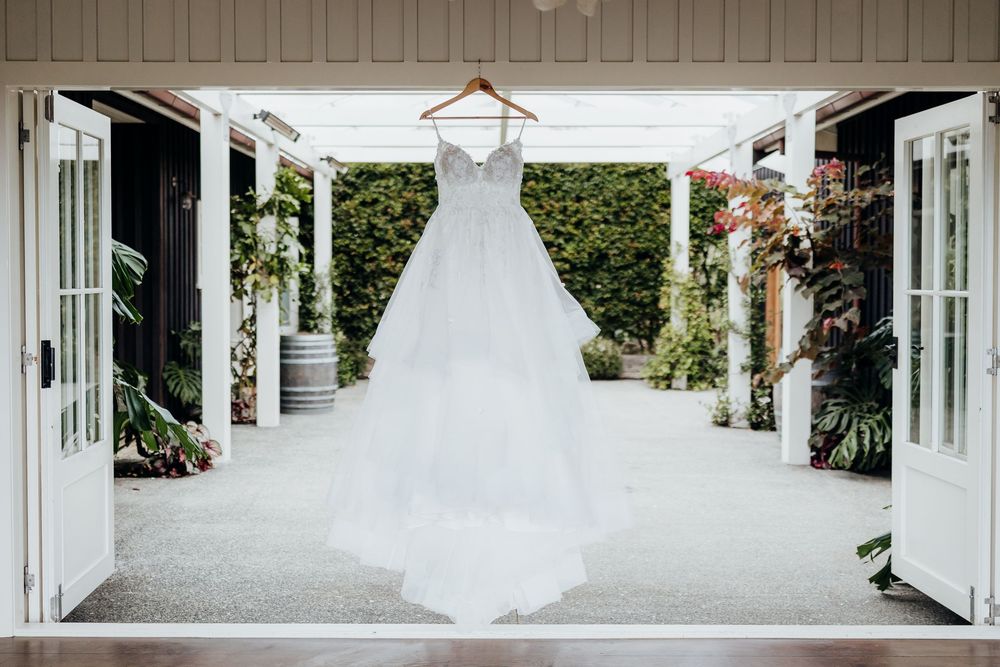 A white wedding dress hangs elegantly in a doorway with French doors and garden views.