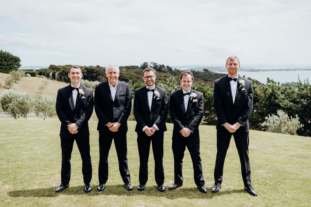 Wedding party in formal attire posing together on grassy hillside.