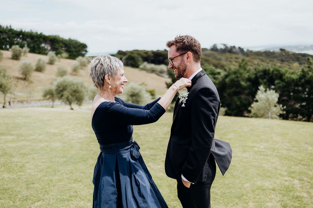 Wedding party members share joyful moments outdoors on a grassy hillside.