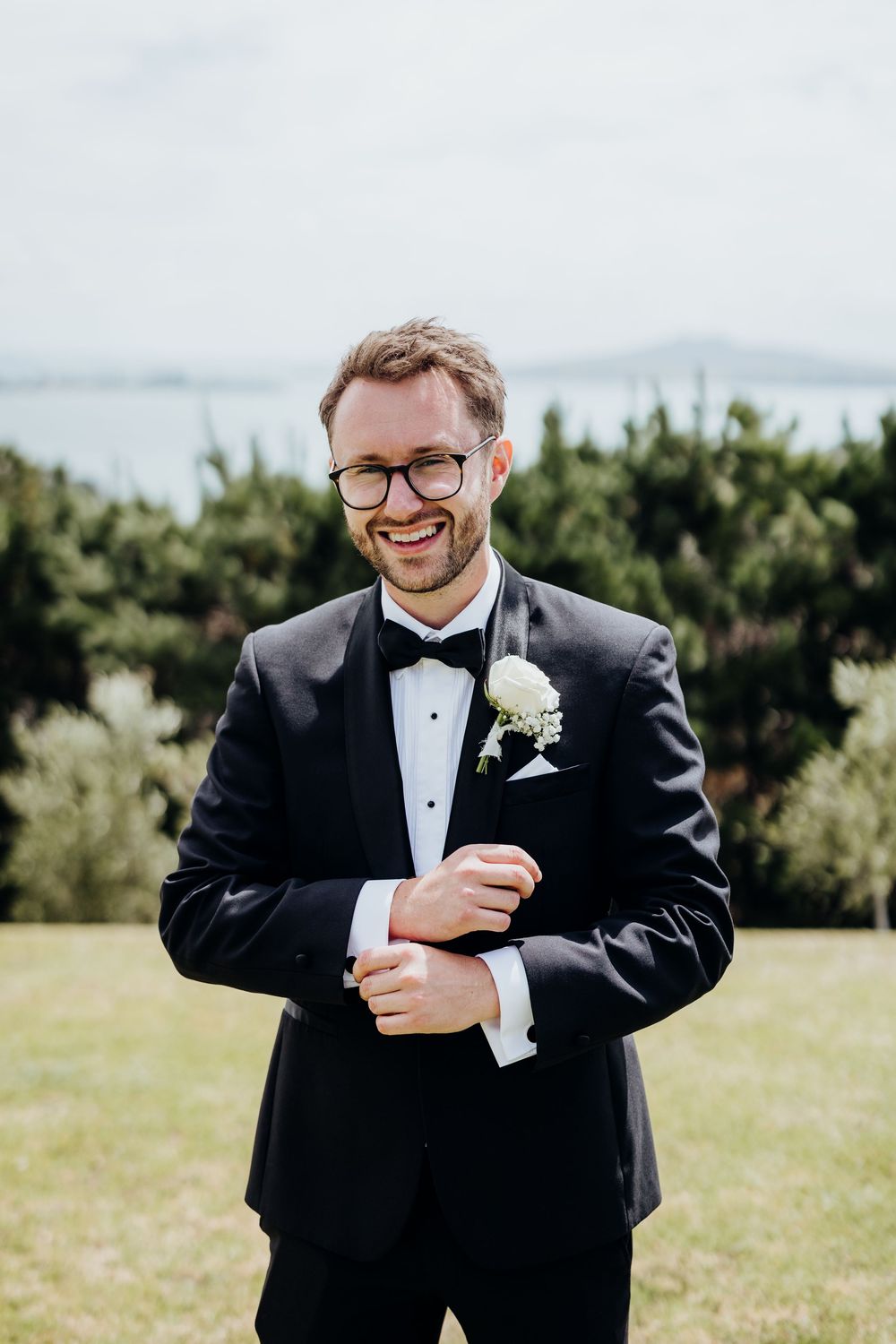 Joyful groom in tuxedo laughing outdoors during wedding photos.