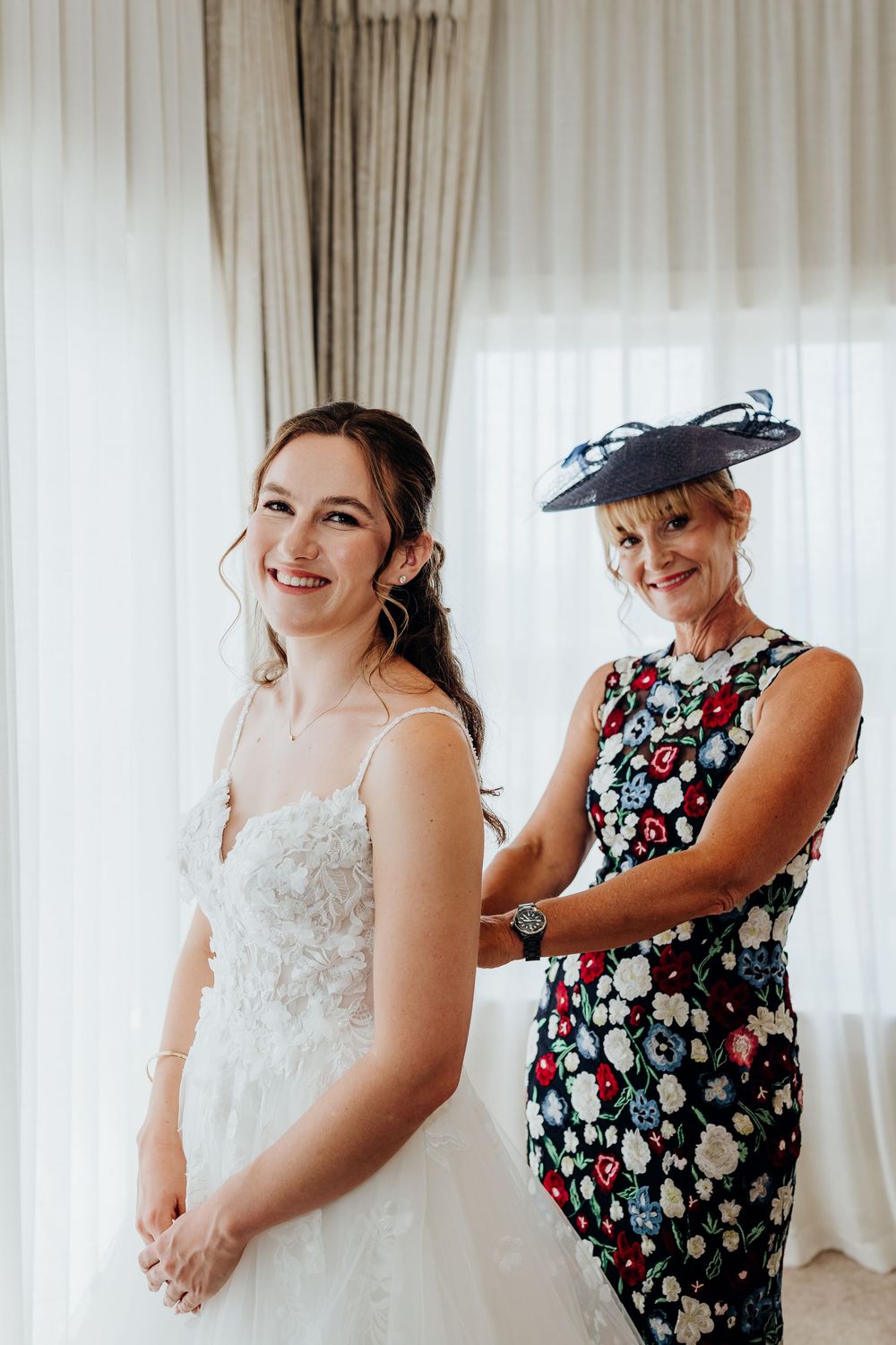 Getting ready scene with bride in wedding dress being assisted with final preparations.