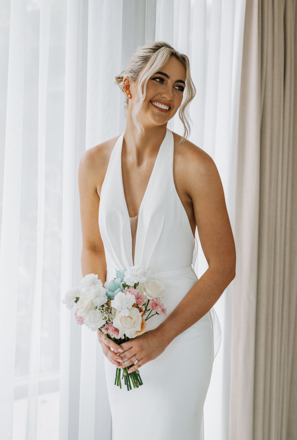 A close-up view of a modern white wedding dress with elegant draping against sheer curtains with natural light.
