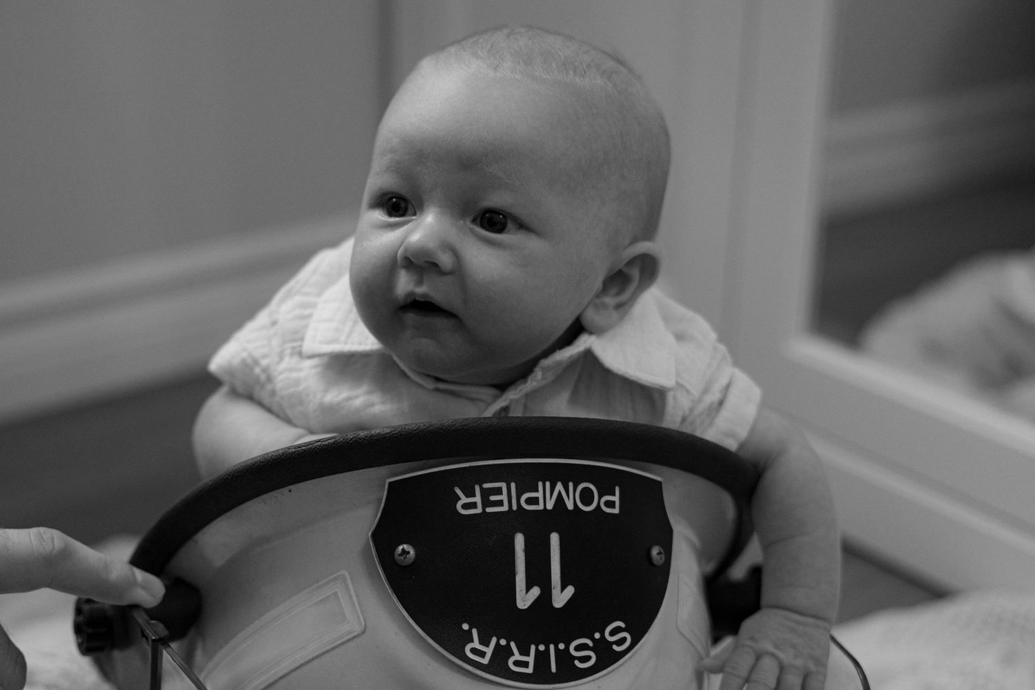 Newborn baby sitting with a firefighter helmet labeled POMPIER in black and white photo.
