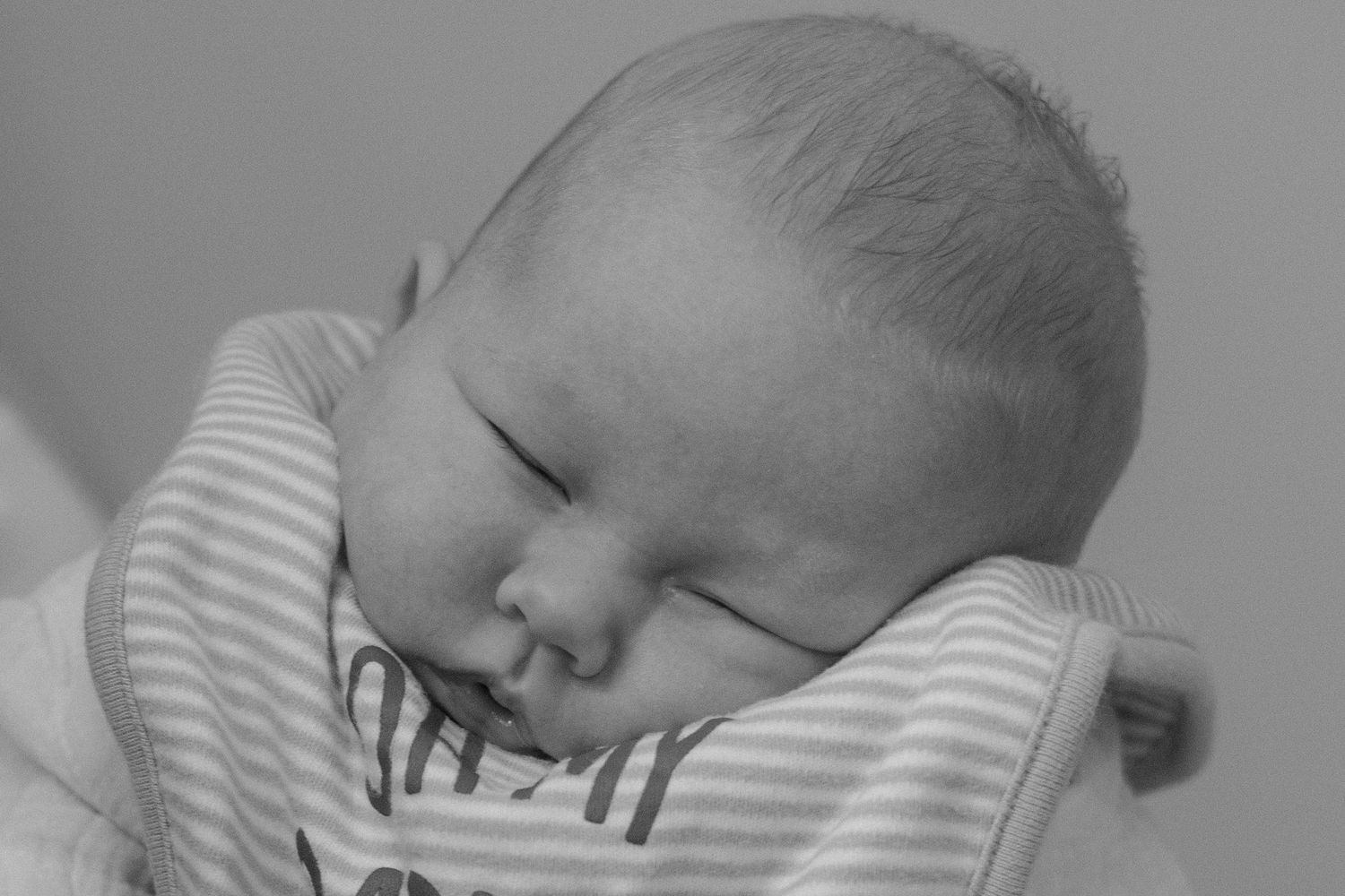 Black and white photo of a peaceful sleeping newborn baby wearing a striped onesie.