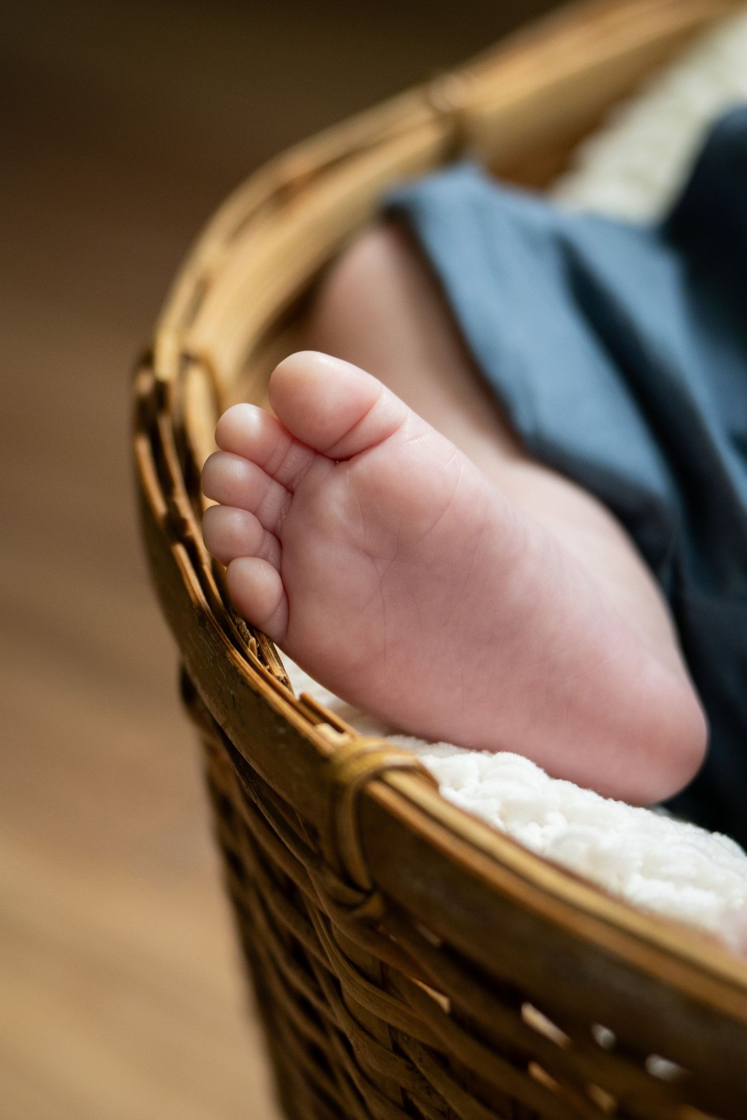Newborn baby's tiny foot peeking out of a wicker basket lined with white fabric.