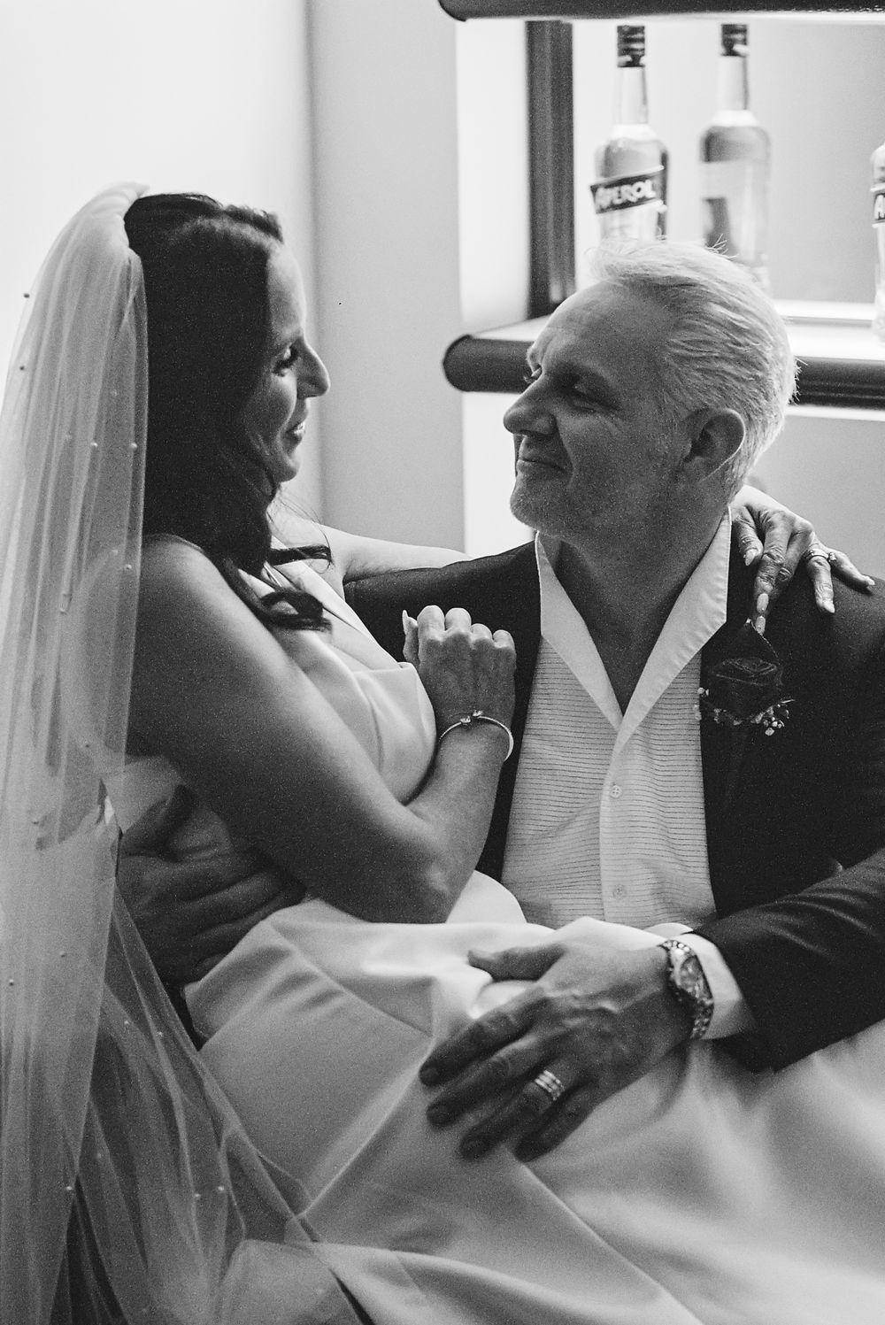 A tender black and white moment between a bride in her wedding veil and an older man sharing an emotional embrace.