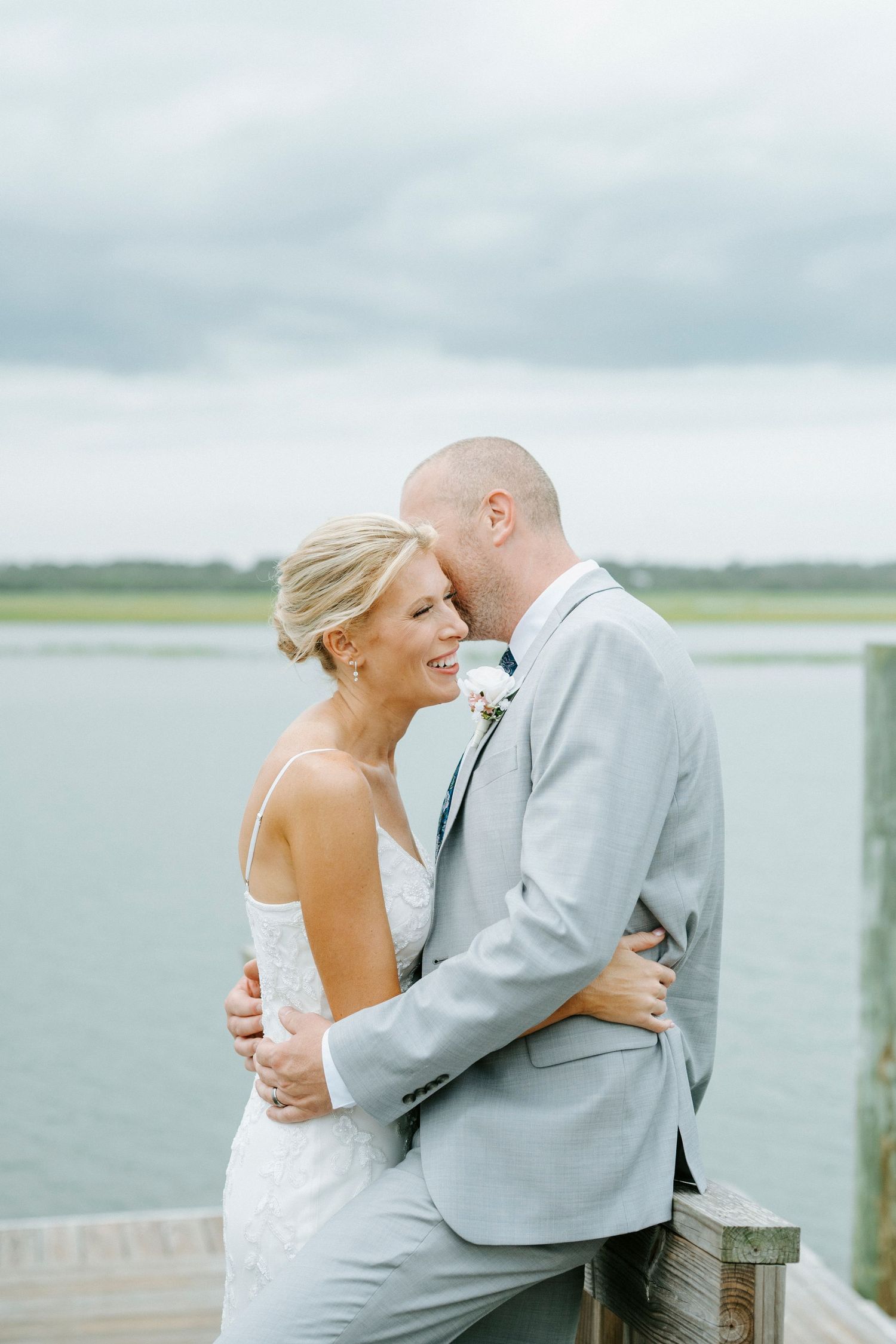 Romantic wedding couple embracing on a dock overlooking a misty lake with overcast skies in the background.