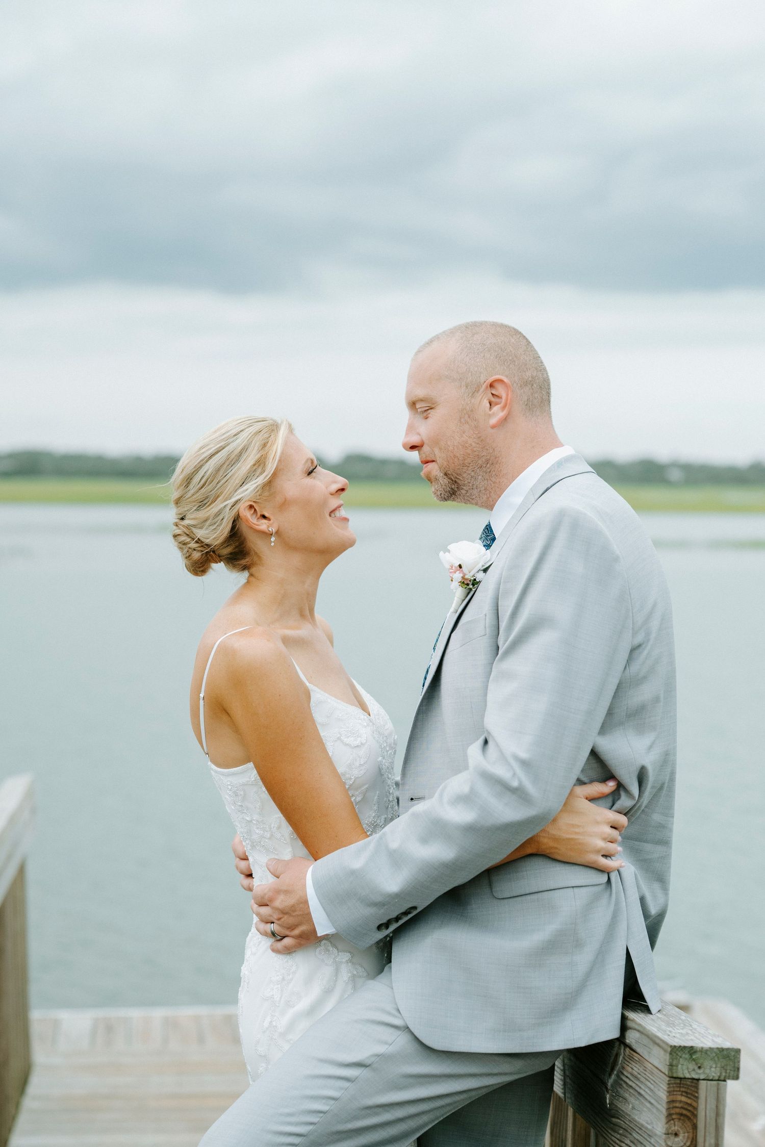 Romantic wedding couple shares intimate moments along a coastal dock on an overcast day.