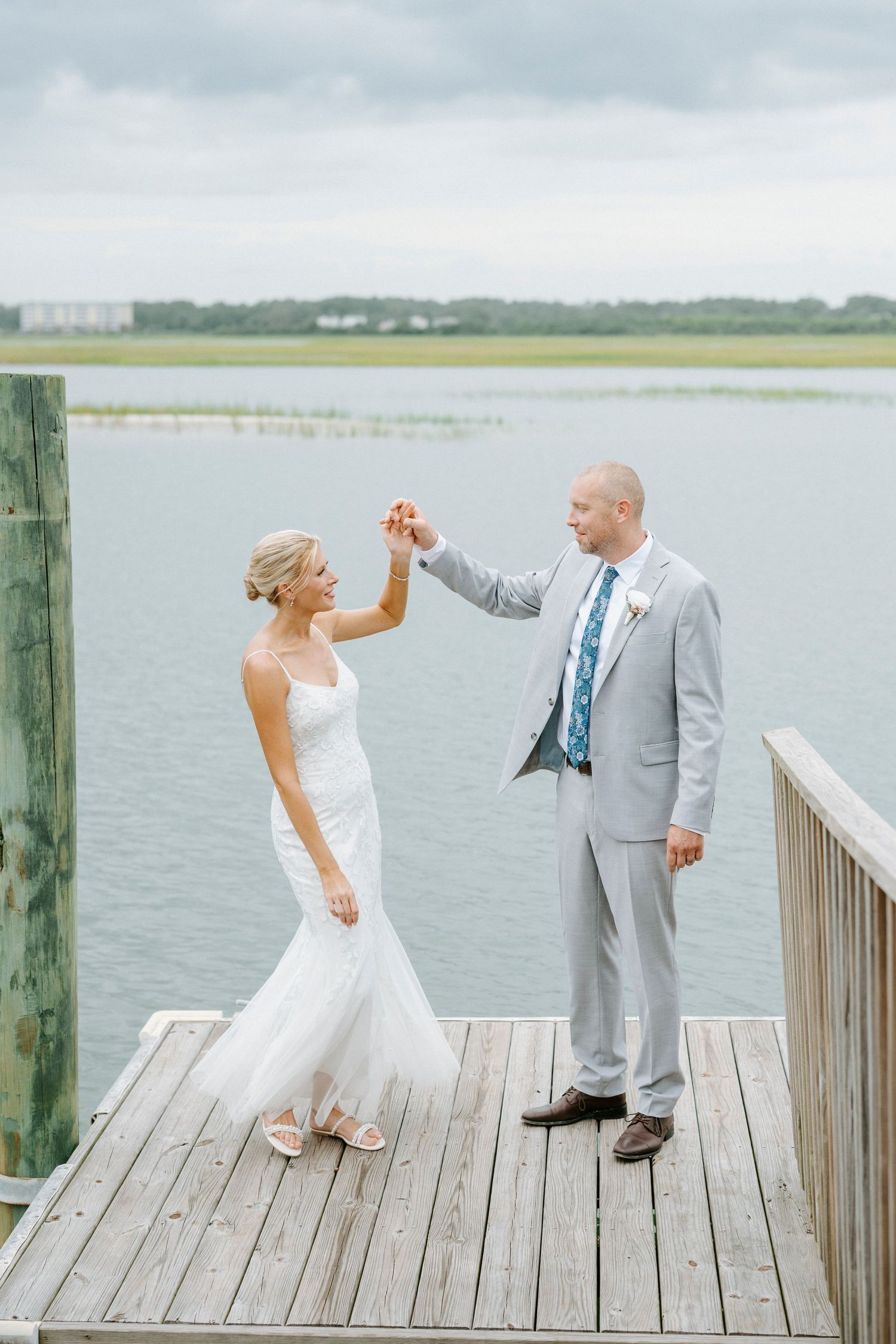 Dancing couple shares a playful moment on a wooden dock by the water during their wedding celebration.