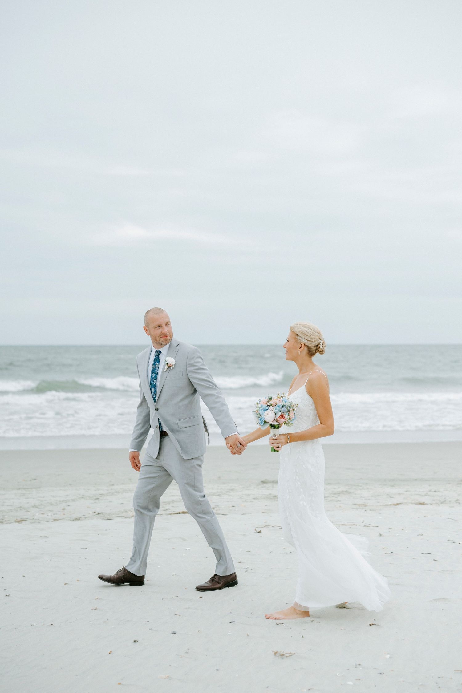 Playful newlyweds dance and twirl together on a misty beach in formal wedding attire.