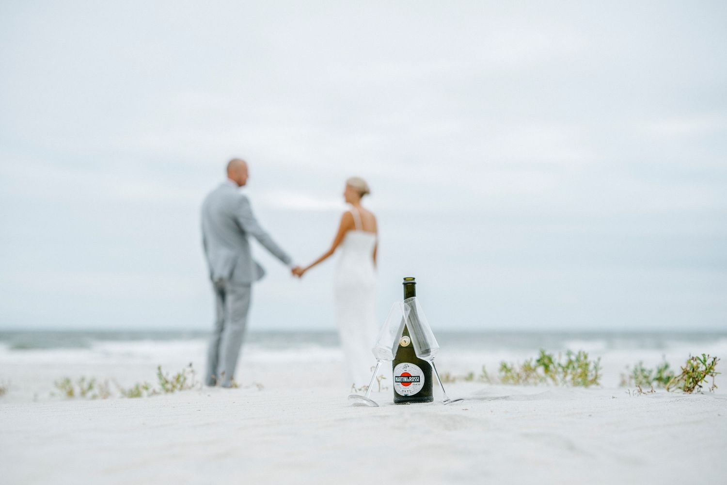 Four artistic wedding photos showing couples on a misty beach with a champagne bottle and romantic poses.