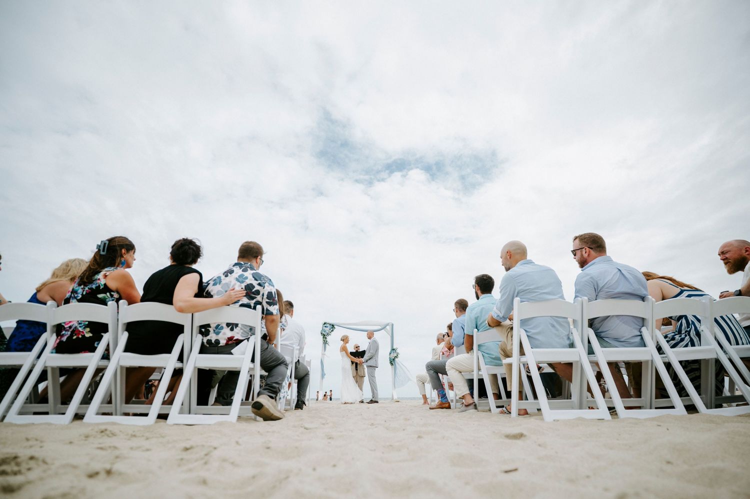 White folding chairs line up on a beach for an outdoor wedding ceremony with ocean views.
