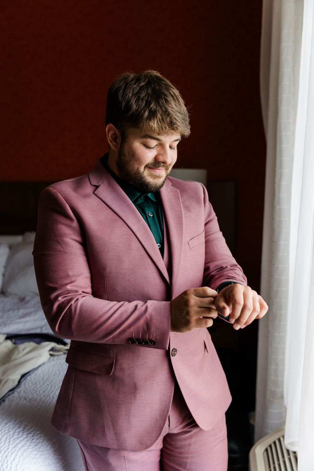 Person wearing a stylish pink suit stands in a naturally lit room with white walls and linens.