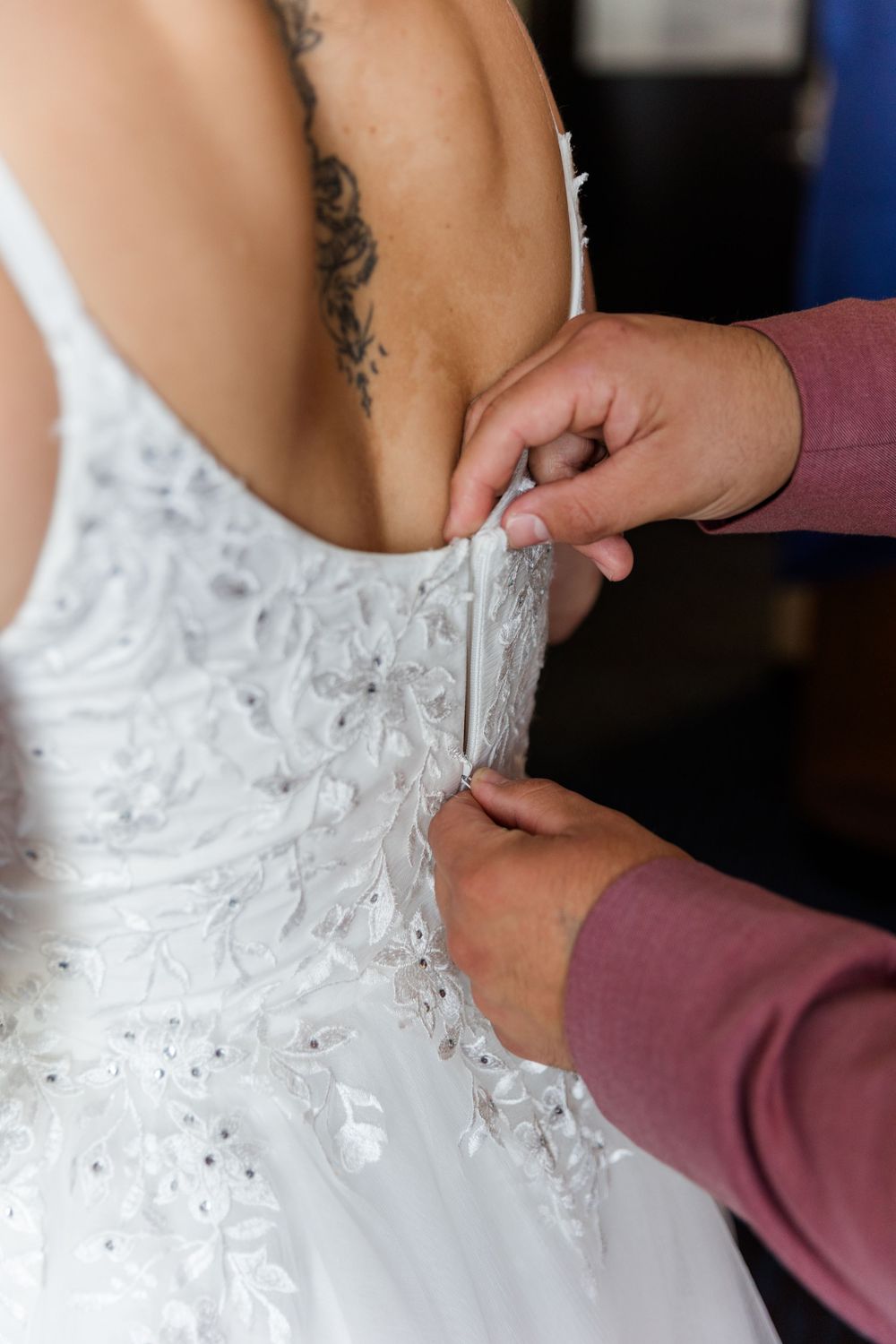 Close-up of wedding dress lacing detail being fastened against white beaded fabric.