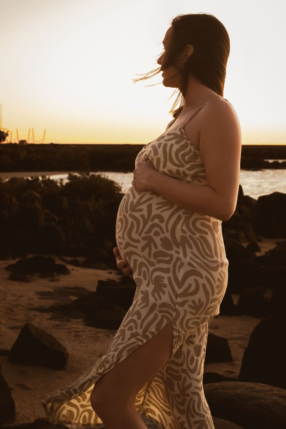 A person in a patterned dress poses against a golden sunset by the ocean.