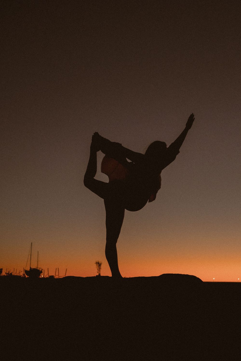 Silhouette of a person performing dance movements at dusk with an orange horizon.