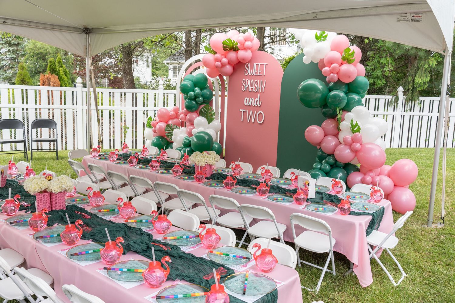 Party tent decorated with pink and green balloon garlands and table settings for an outdoor celebration.